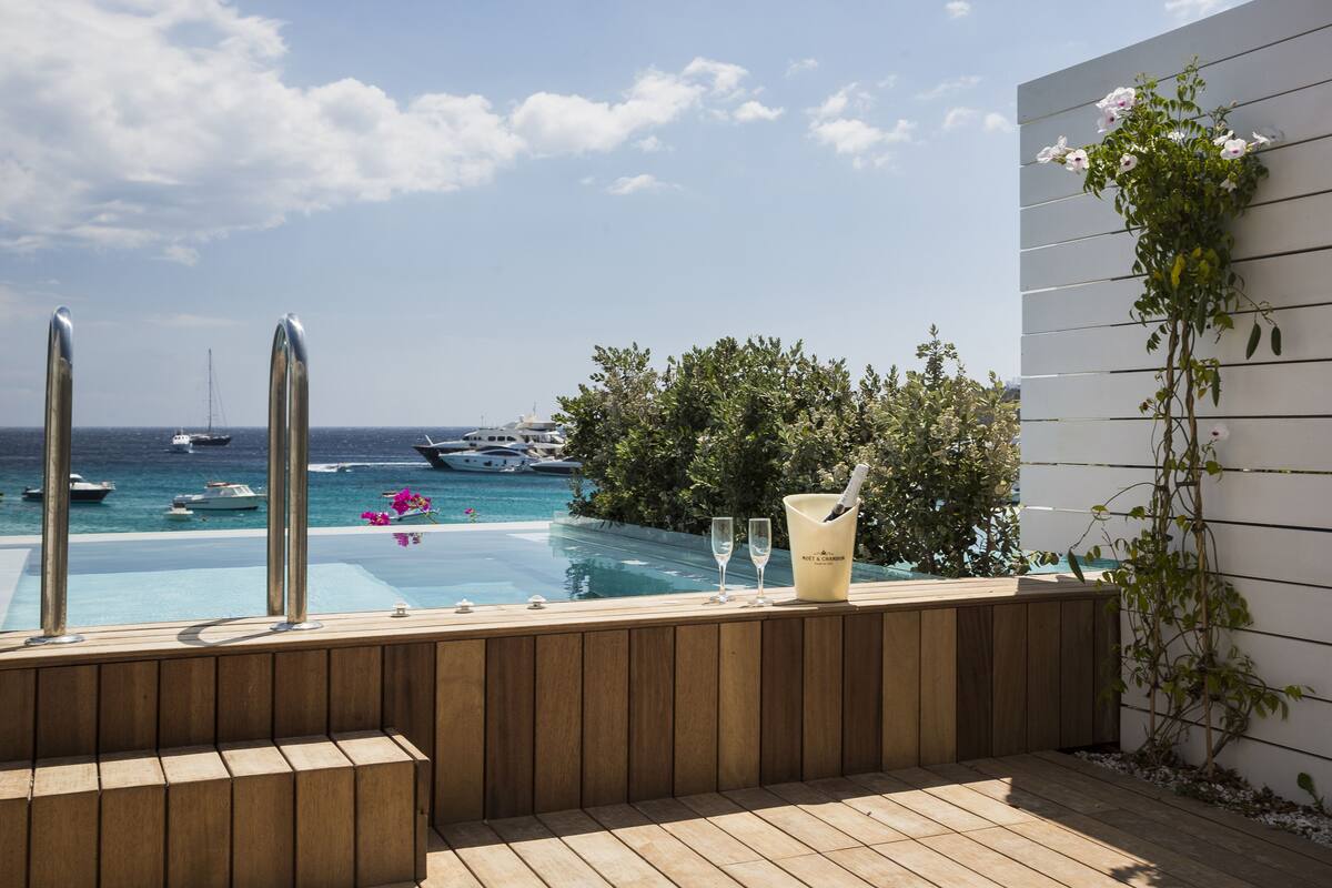 Terraza de madera con piscina, con vista al mar y barcos.