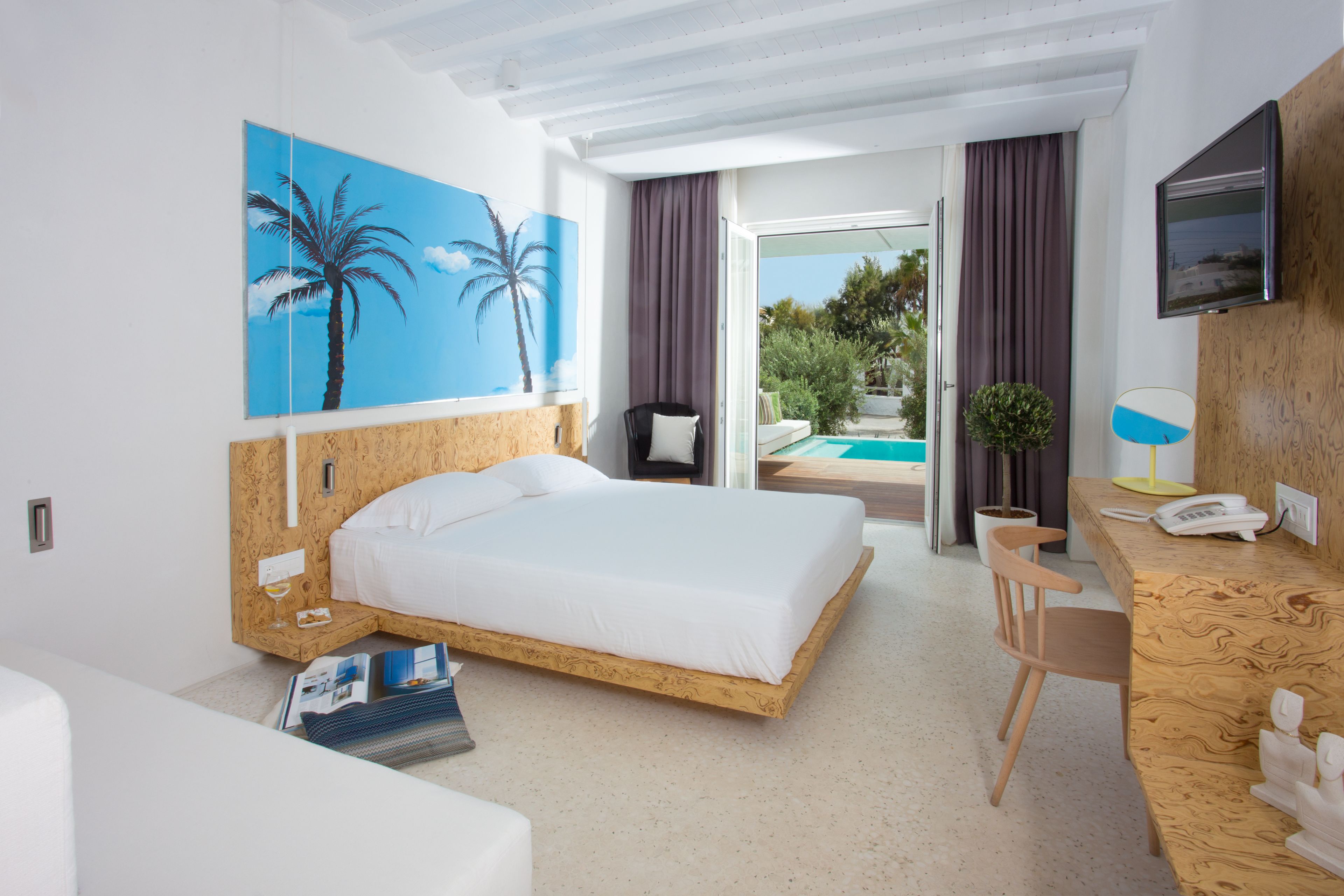 Habitación de hotel moderna con una cama grande, un escritorio, un televisor y vistas al área de la piscina exterior.