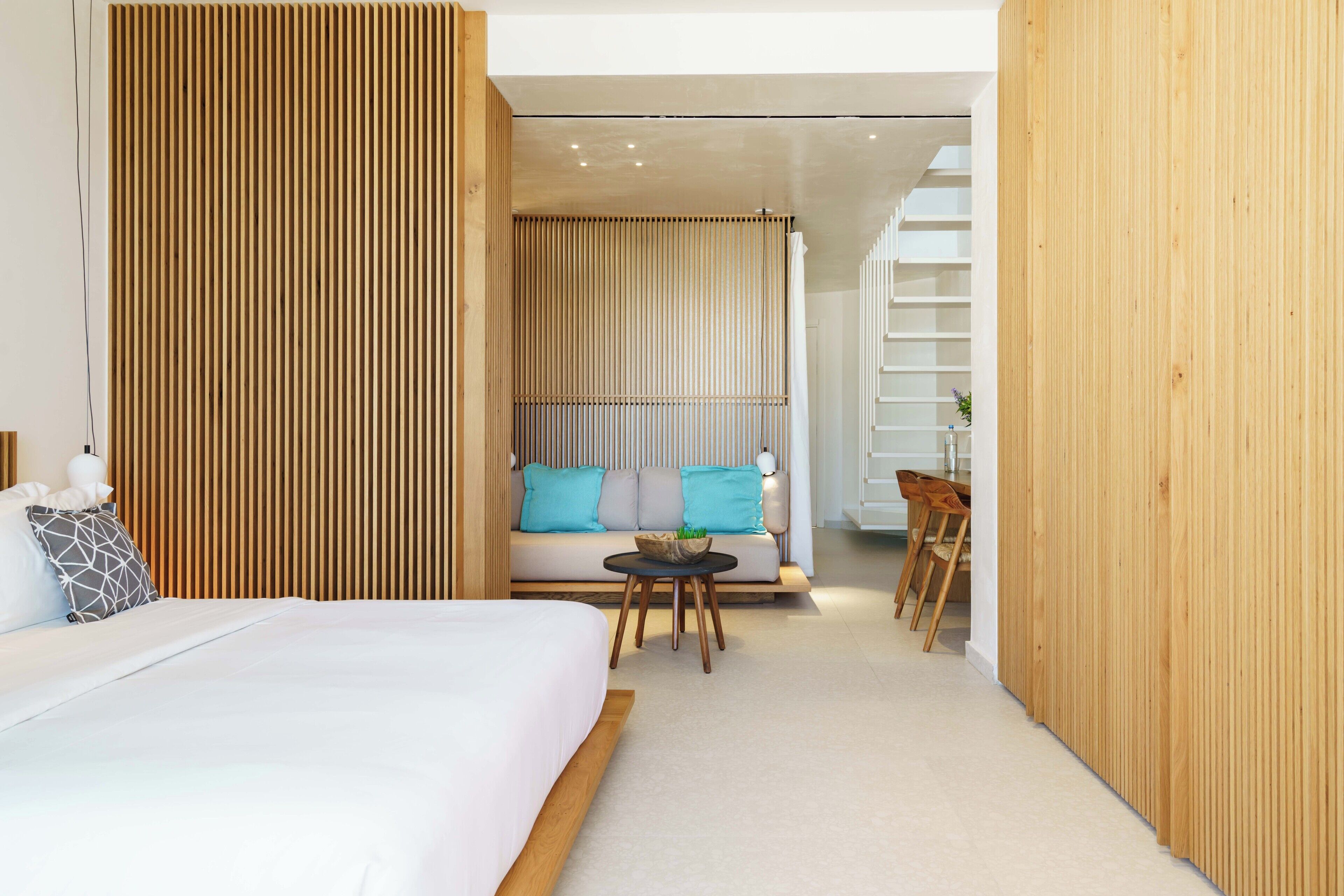 Una habitación de hotel moderna con una cama grande, una mesita con un cuenco, un sofá con cojines y un separador de madera.