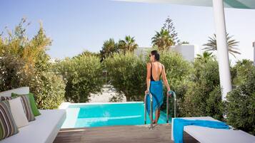 Un espace aménagé au bord de la piscine, avec une terrasse en bois, des chaises longues et une personne qui se dirige vers la piscine.