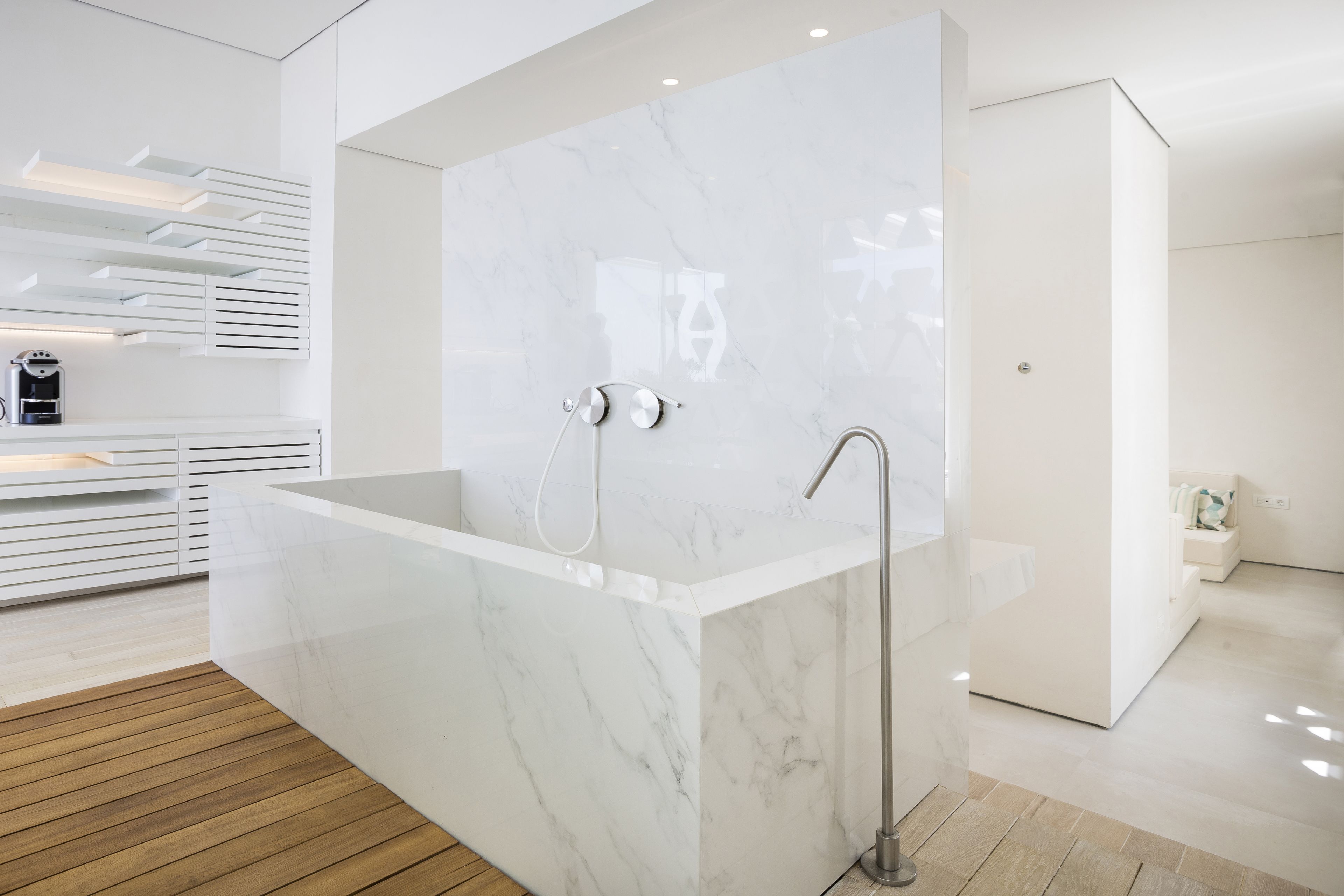 A modern bathroom with a large marble bathtub, a wooden floor, and a minimalist design.
