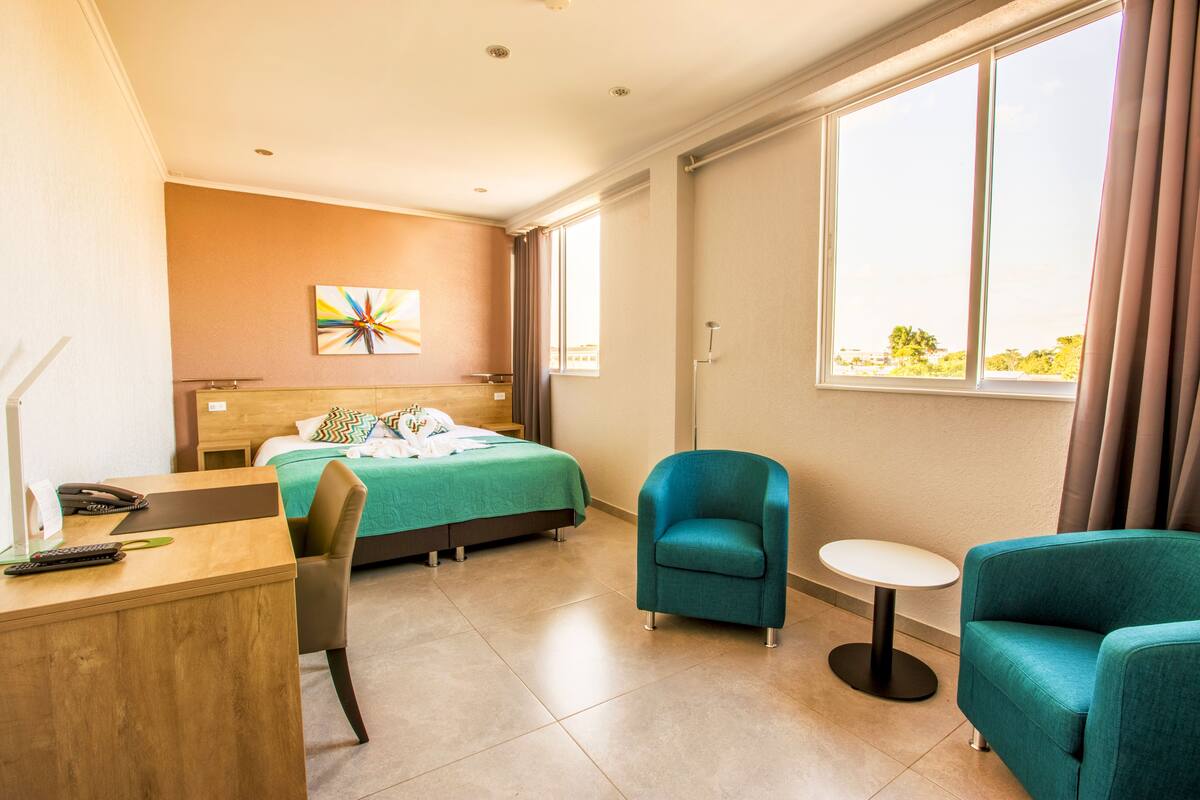 A hotel room with a bed, a desk, a chair, a small table, and a window with curtains.