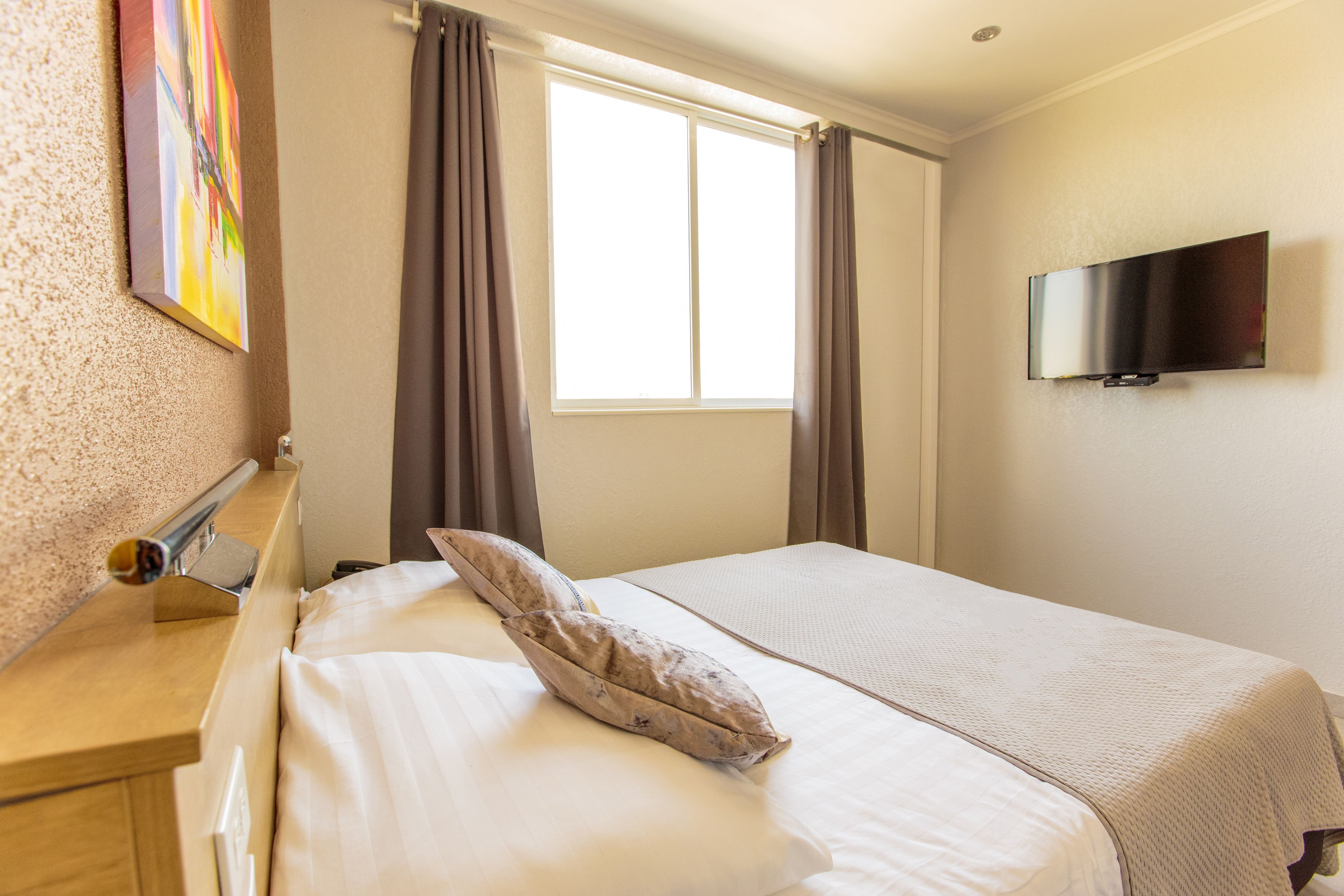 Habitación de hotel con cama, televisor en la pared y ventana con cortinas.