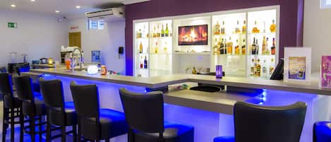 A bar area with a long counter, multiple bar stools, and a television screen displaying a fire.