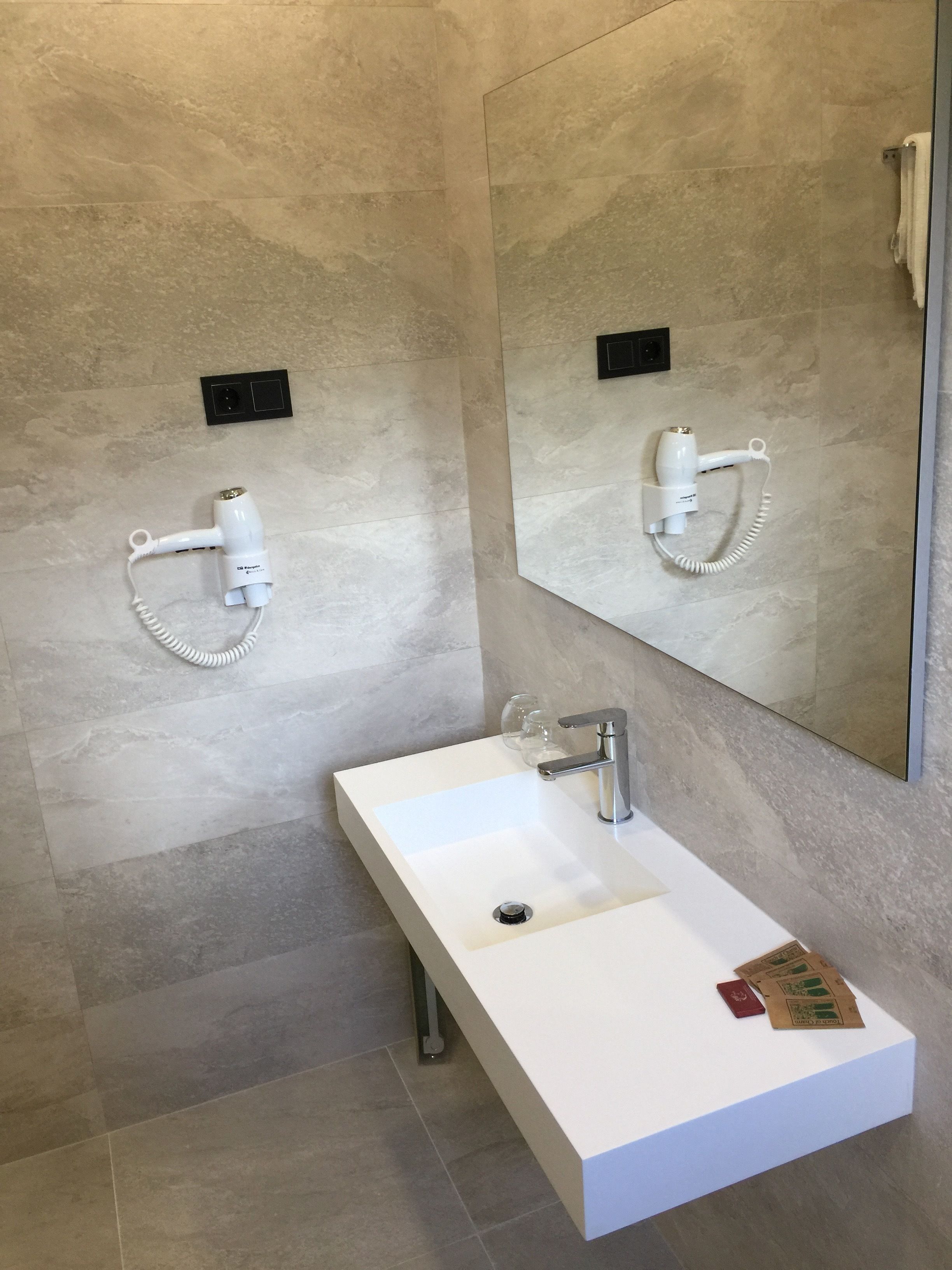 Un baño moderno con un lavamanos blanco, un espejo y dos secadores de pelo montados en la pared.