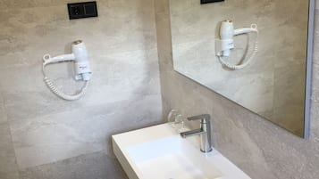 Un baño moderno con un lavamanos blanco, un espejo y dos secadores de pelo montados en la pared.