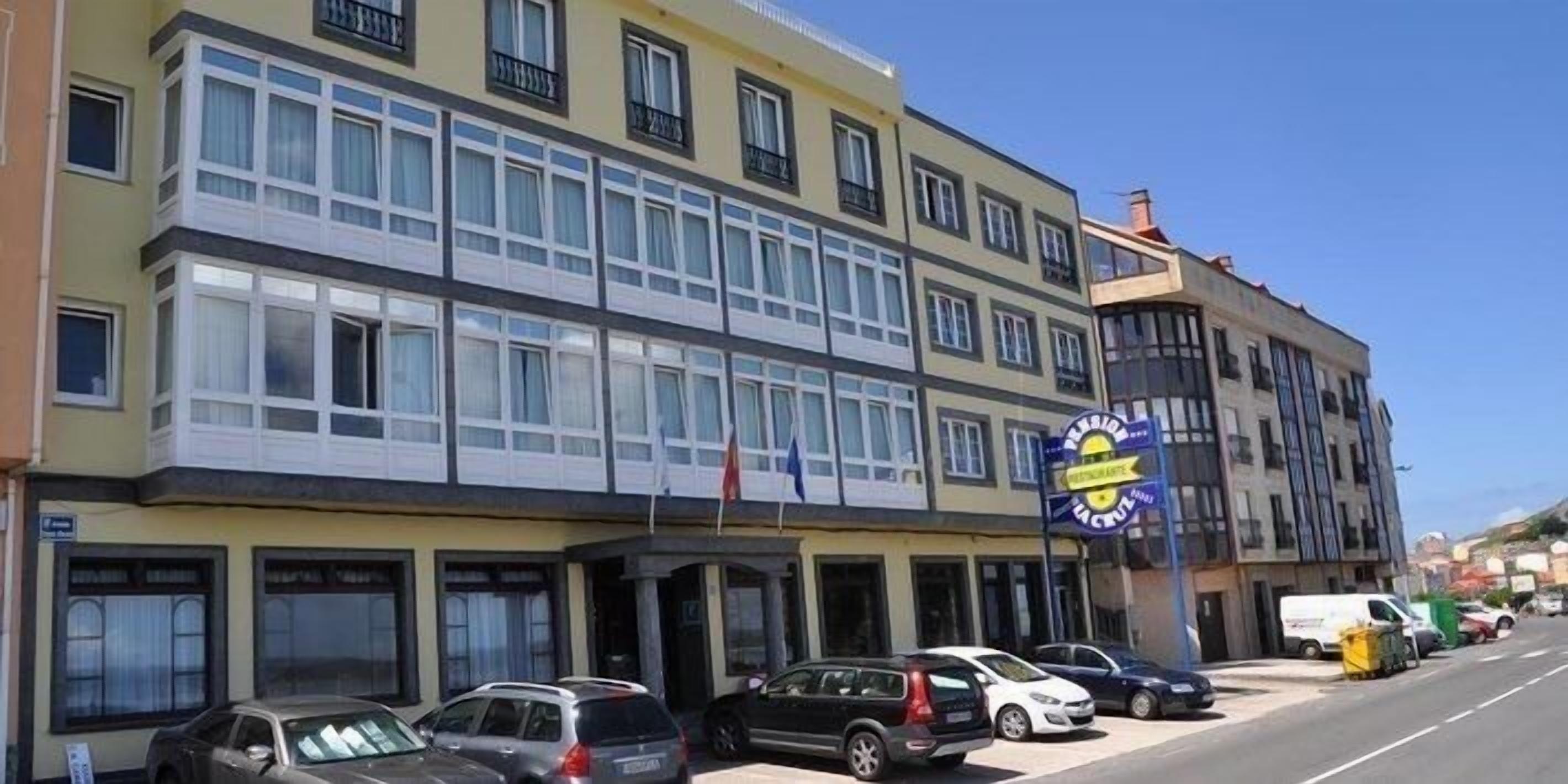 Un edificio de varios pisos con fachada amarilla, varias tiendas en la planta baja y un estacionamiento con coches.