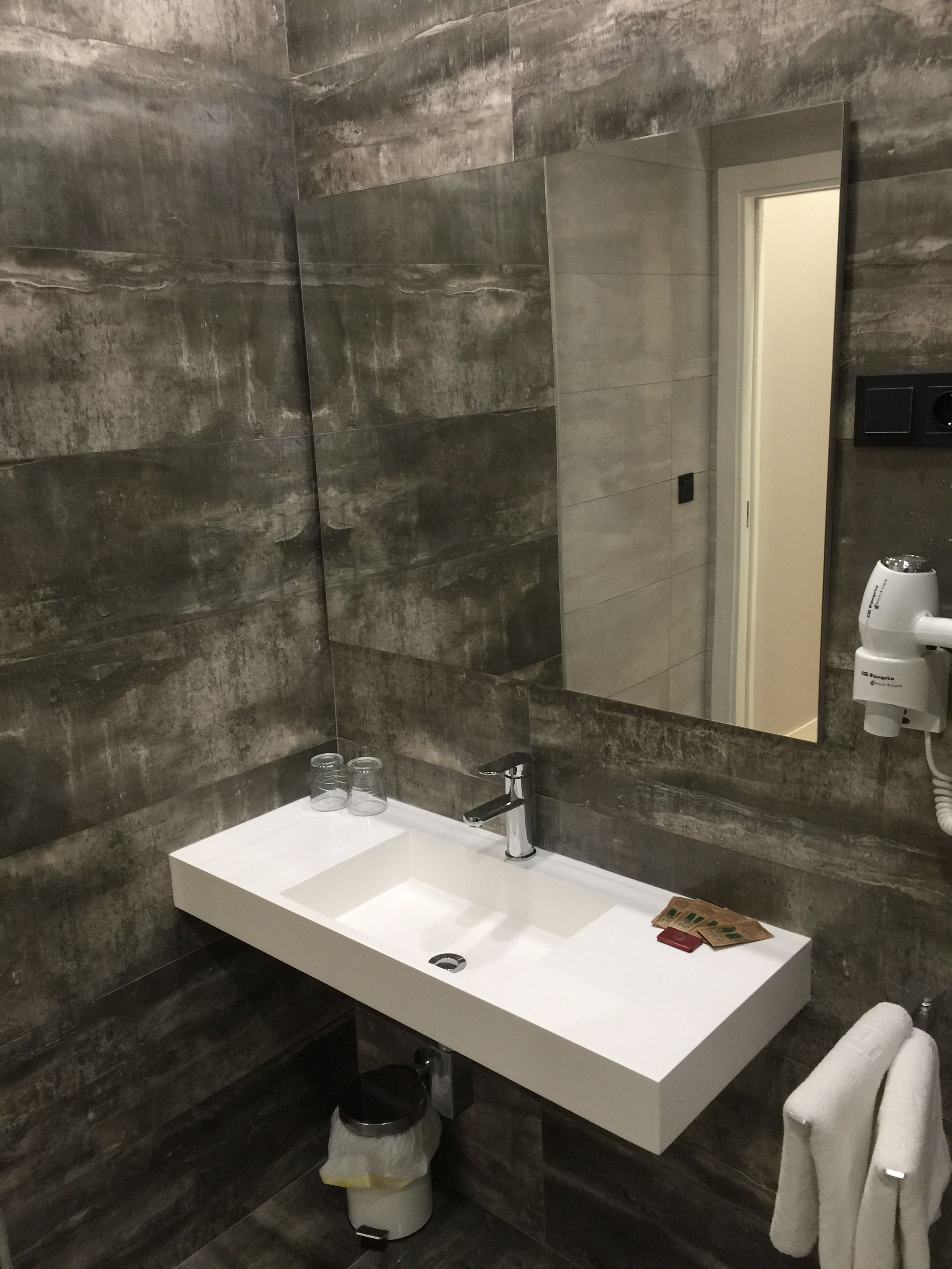 A modern bathroom with a rectangular white sink, a handheld mirror, and a towel rack.