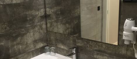 A modern bathroom with a rectangular white sink, a handheld mirror, and a towel rack.