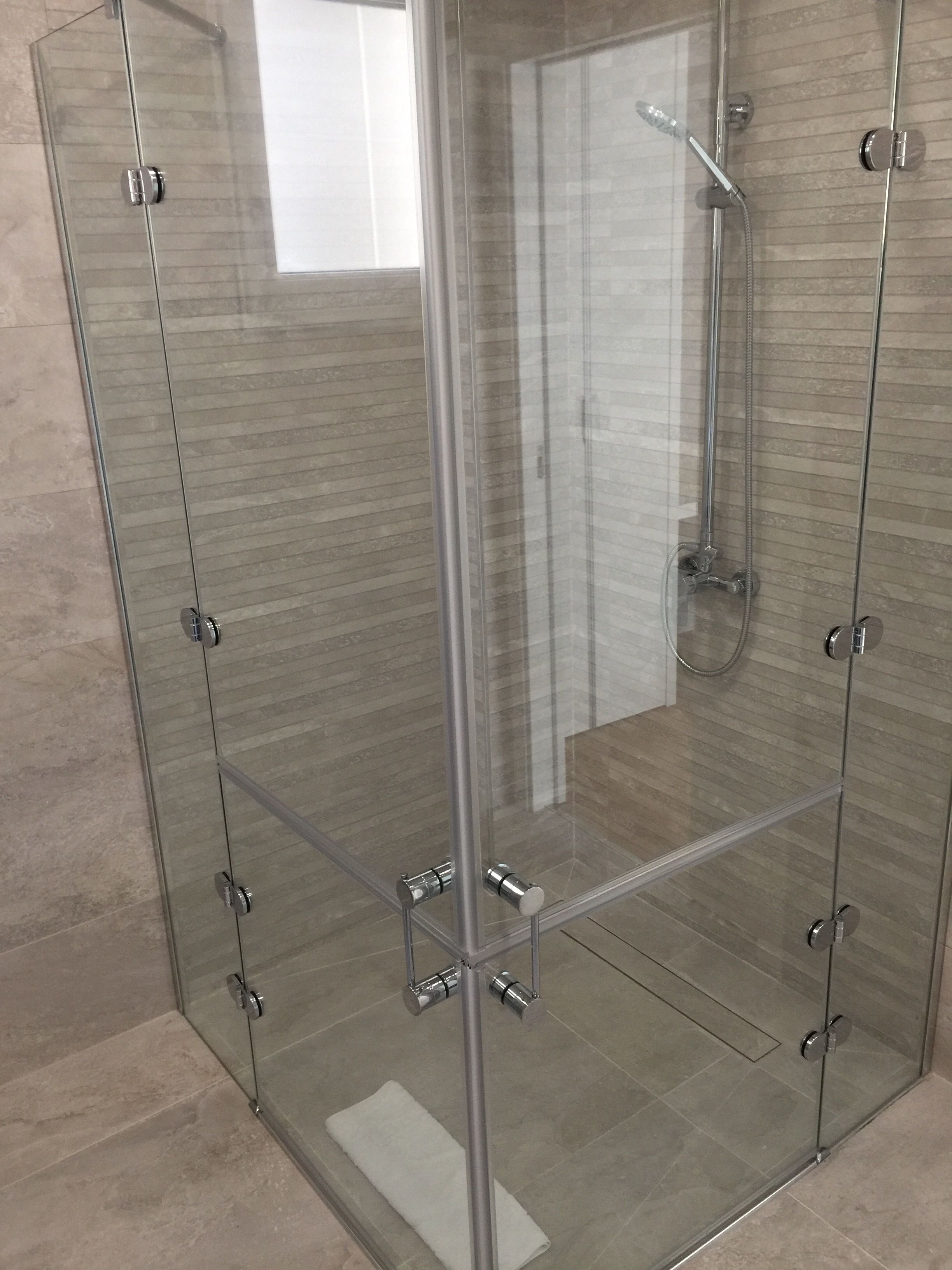 A glass-enclosed shower with a handheld showerhead and a handheld shower attachment.