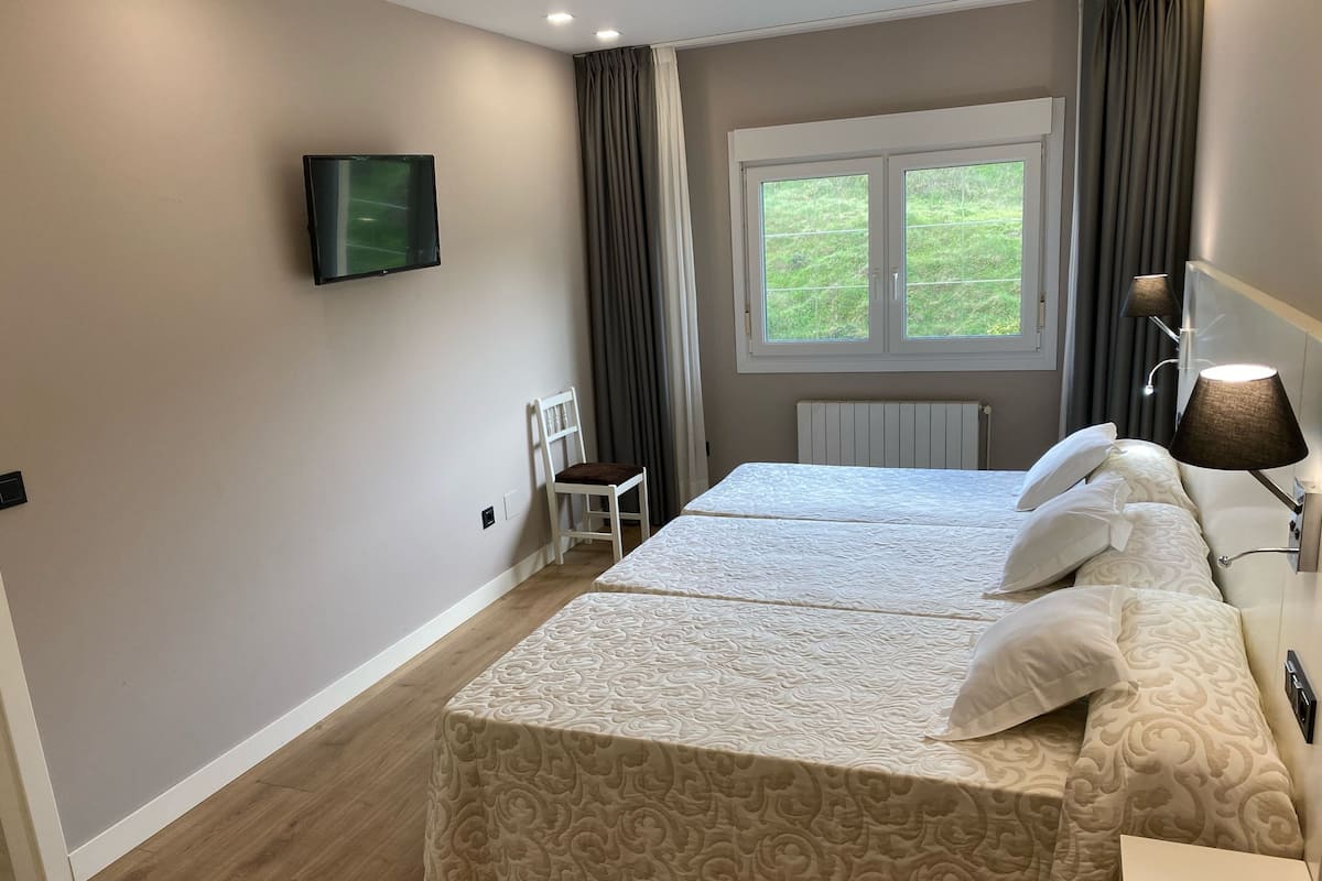 Quarto de hotel com duas camas, televisão, uma cadeira, janela com cortinas e abajur.