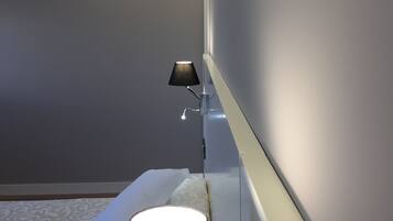 A modern hotel room with a bed, a bedside table with a lamp, and a wall-mounted light fixture.