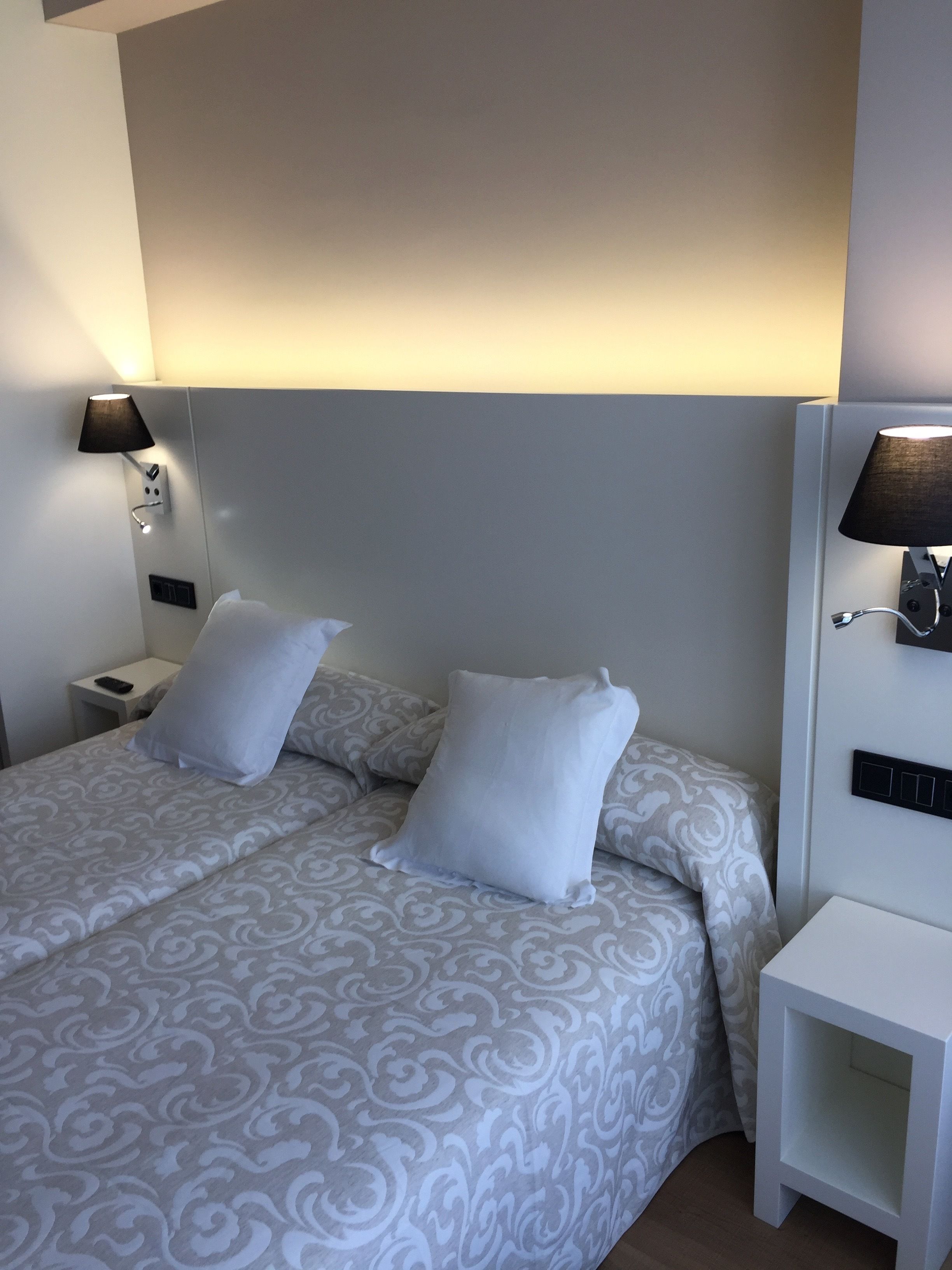 A double bed with patterned bedding, two bedside lamps, and a white nightstand.