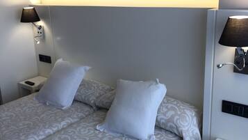 A double bed with patterned bedding, two bedside lamps, and a white nightstand.