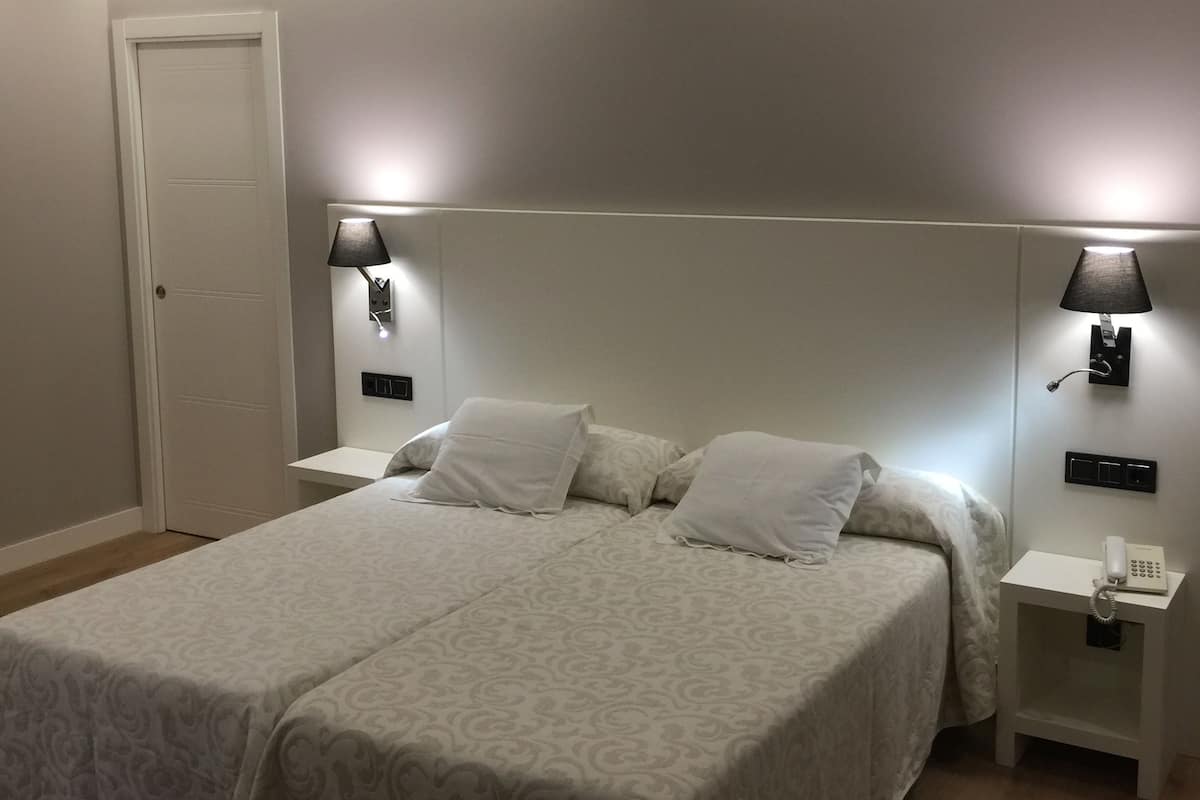 Quarto com uma cama grande, duas mesas de cabeceira com luminárias, uma porta branca e um telefone fixado na parede.
