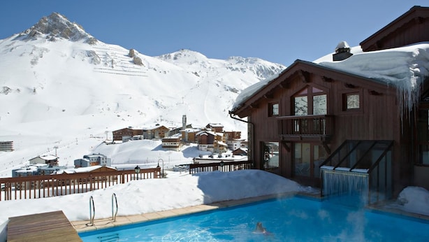 Un área de piscina con terraza de madera, un jacuzzi y vistas a montañas nevadas.