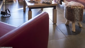 Una sala de estar acogedora con chimenea, un sofá rojo, una mesa de centro de madera y vistas a montañas a través de amplios ventanales.