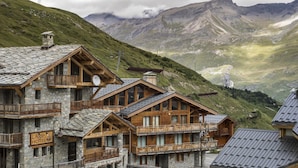Un refugio de montaña con construcción de piedra y madera, balcones de madera y un letrero que indica que es un hotel.