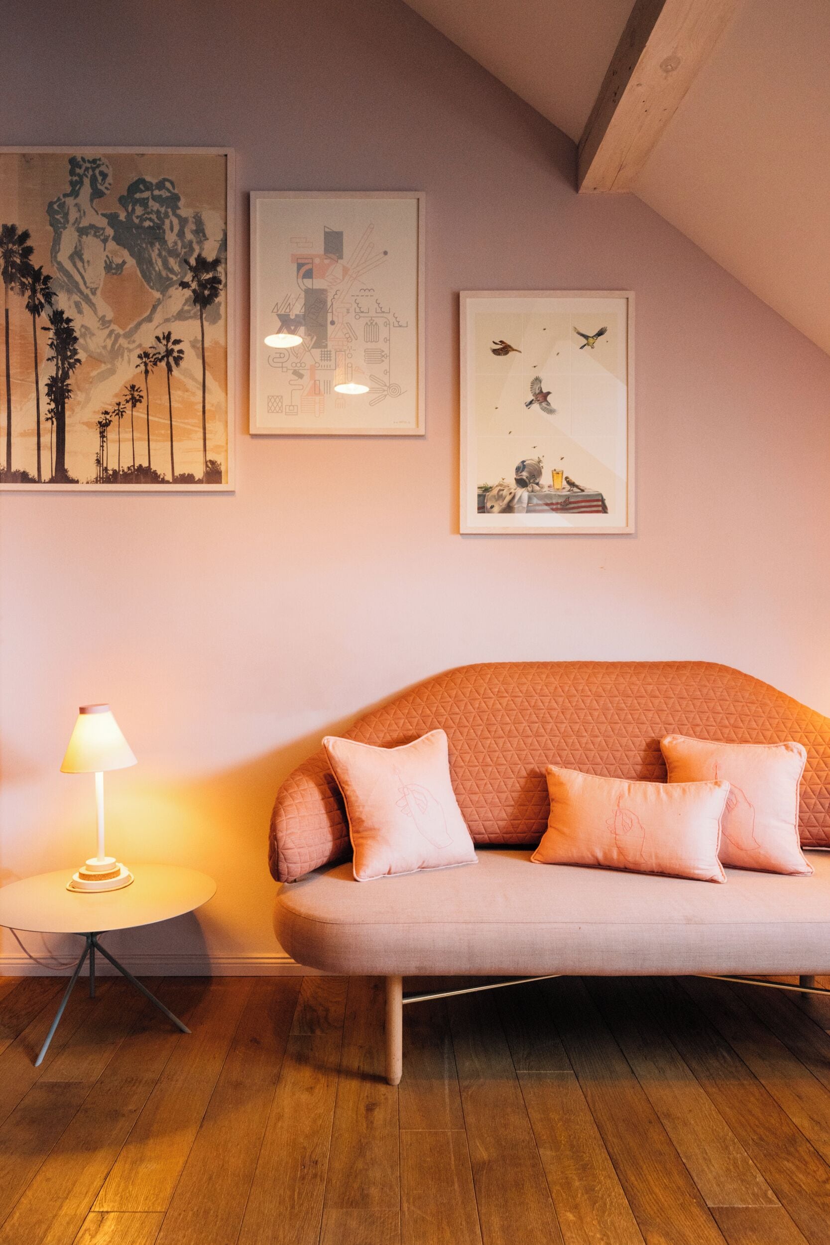 Una habitación acogedora con un sofá mullido, una pequeña mesa redonda con una lámpara y tres cuadros enmarcados en la pared.