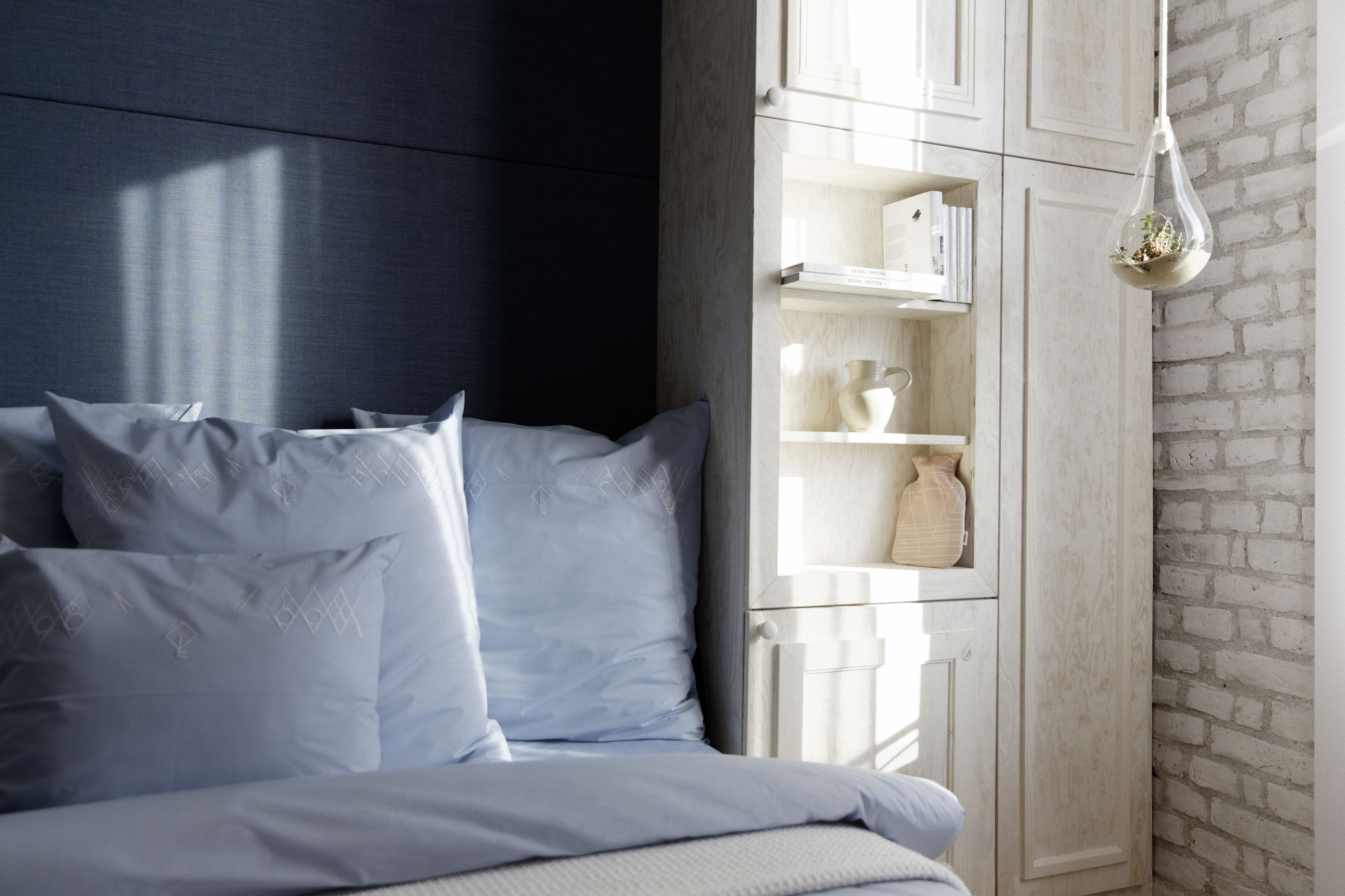 Un dormitorio con una cama, almohadas, una mesita de noche, un armario blanco con estantes y una lámpara colgante.