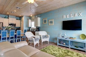 A modern kitchen with white cabinets, a microwave, and a dining area with blue chairs. - Bonzai Bay SP1 2 8 9 (Port Aransas)