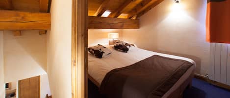 Un dormitorio con techo de madera, una cama con manta marrón, una mesita de noche con lámpara y un armario.