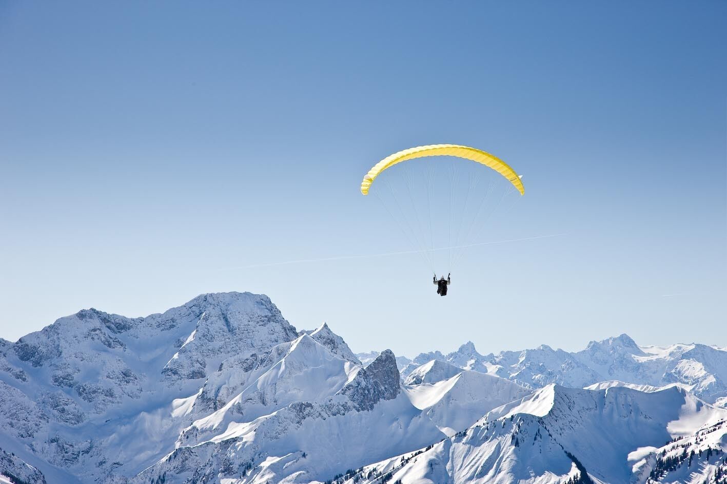 En person paraglider over et snedækket bjerglandskab.