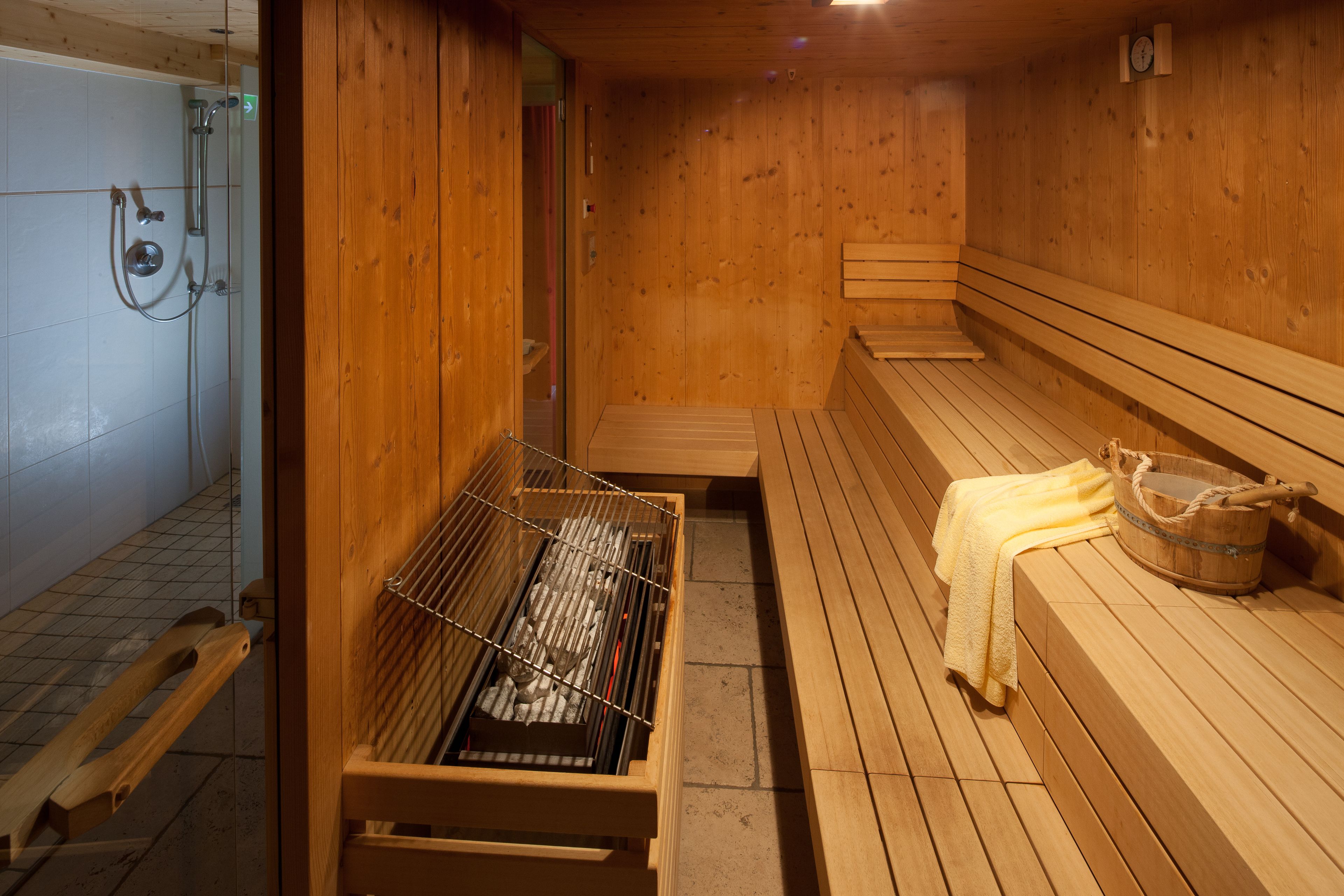Una sauna con bancos de madera, un banco de madera con una toalla y un cubo de madera.