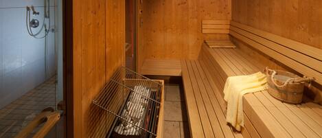Una sauna con bancos de madera, un banco de madera con una toalla y un cubo de madera.