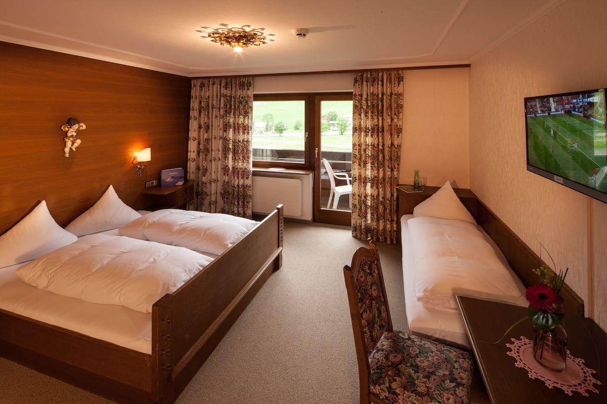 A hotel room with two beds, a desk, a chair, a TV, and a view of the outdoors.