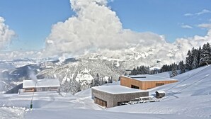 A snow-covered mountain landscape with modern buildings, including a wooden structure and a brick building with a snow-covered roof. - Hotel Elisabeth (Schoppernau)