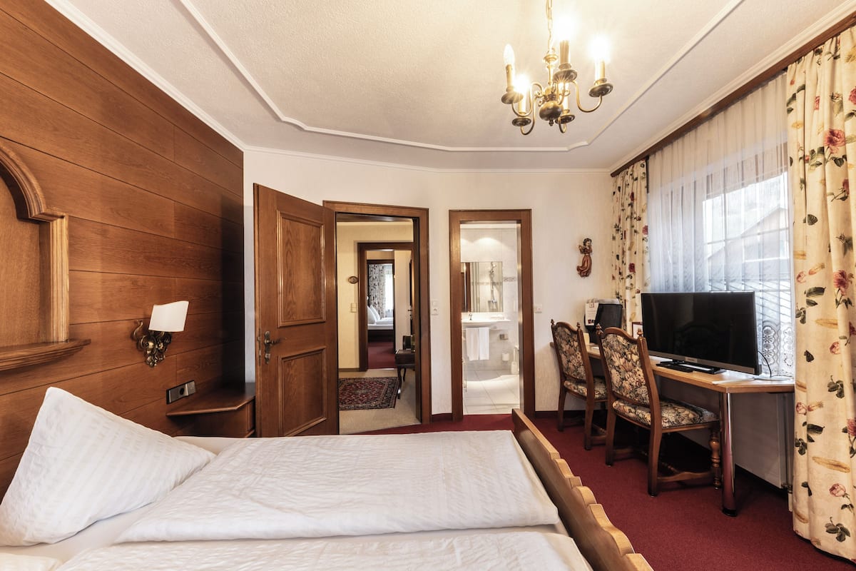 A hotel room with a wooden headboard, a bed with white linens, a desk with a computer, a television, and a floral curtain.
