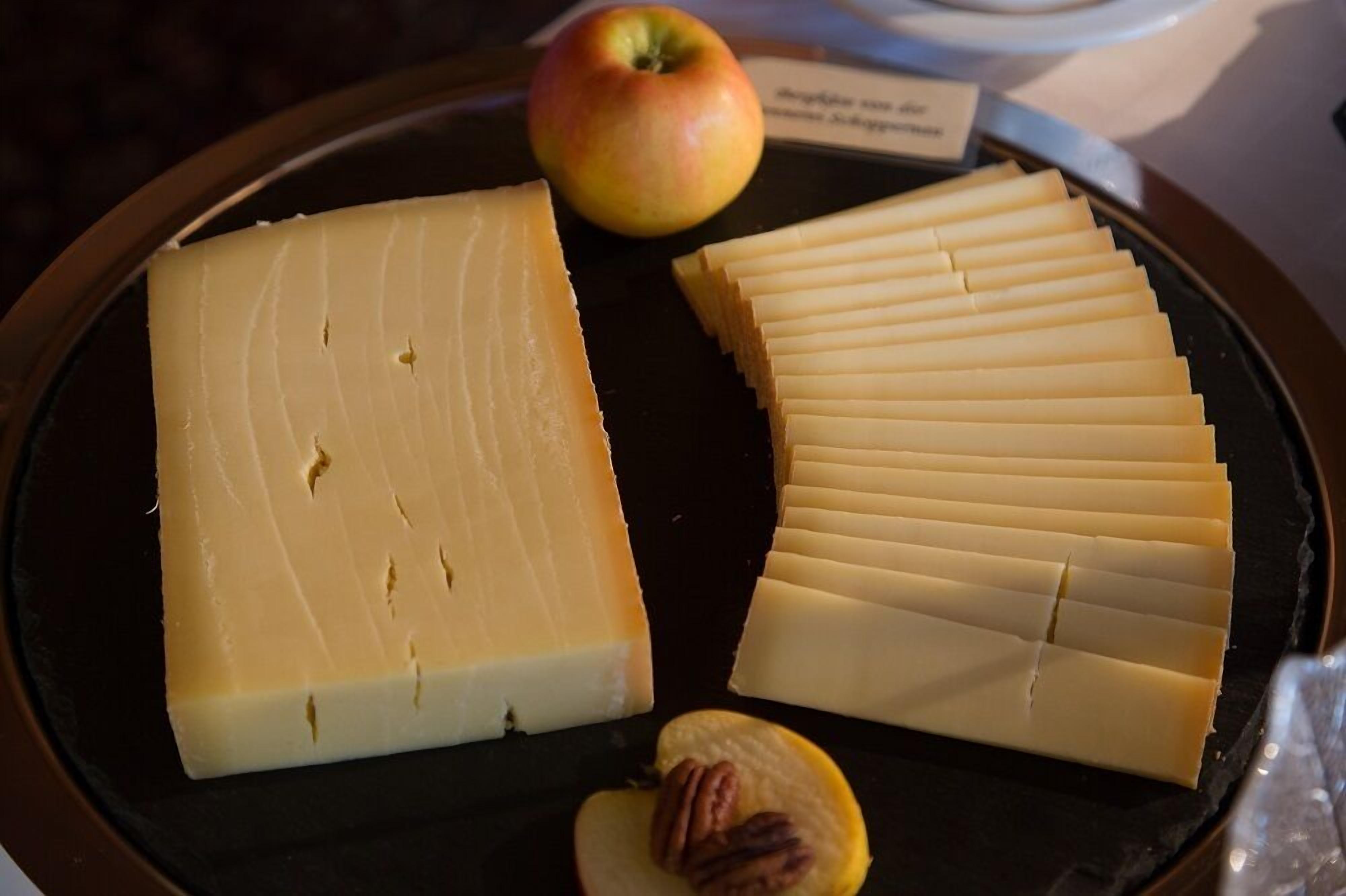 Un plateau de fromages comprenant une grosse part de fromage, des tranches de fromage fines et une pomme.
