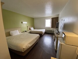 Habitación de hotel con dos camas, un escritorio, un refrigerador y una ventana con cortinas.