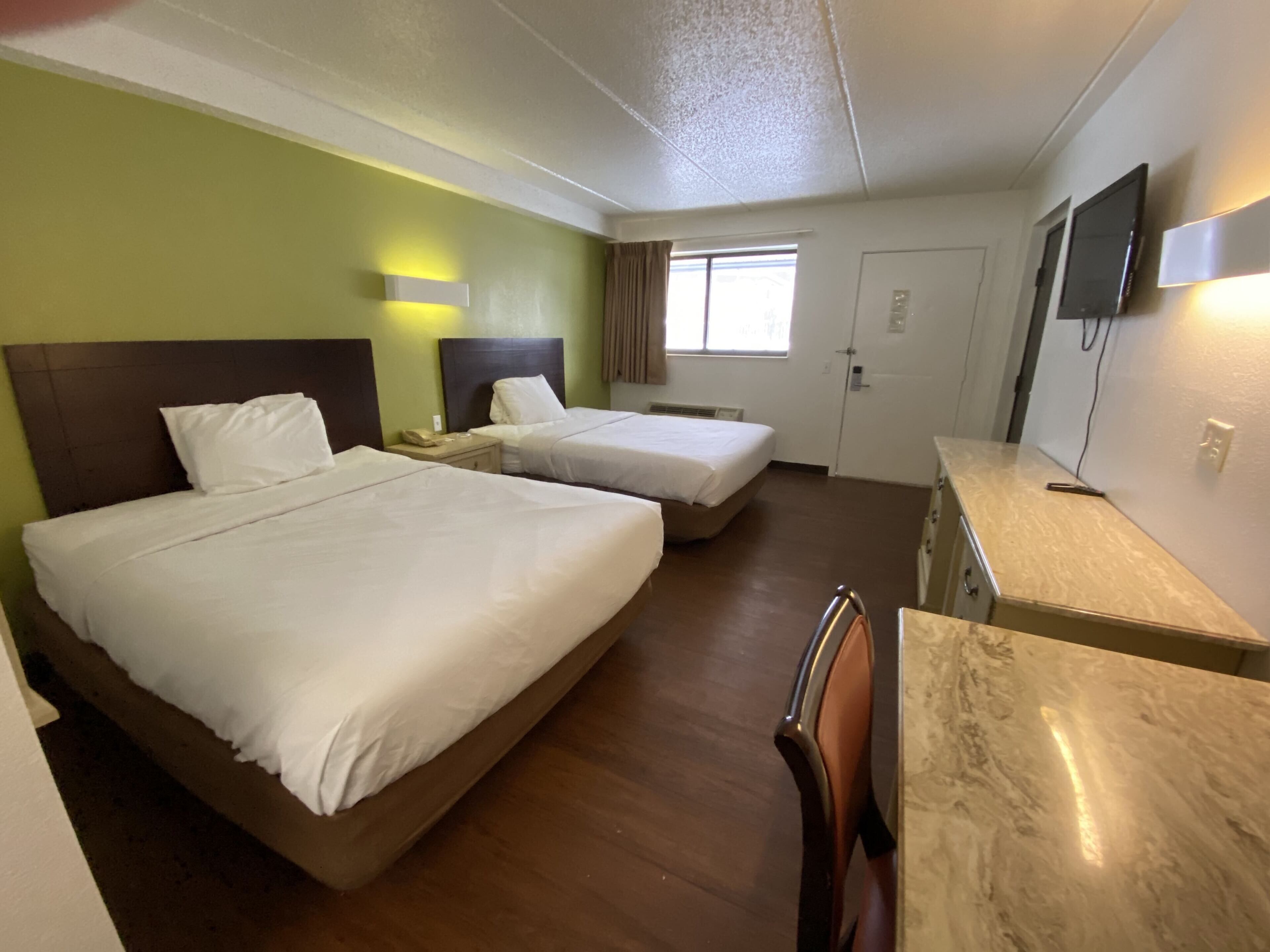 A hotel room with two beds, a desk, a chair, a TV, and a window with curtains.
