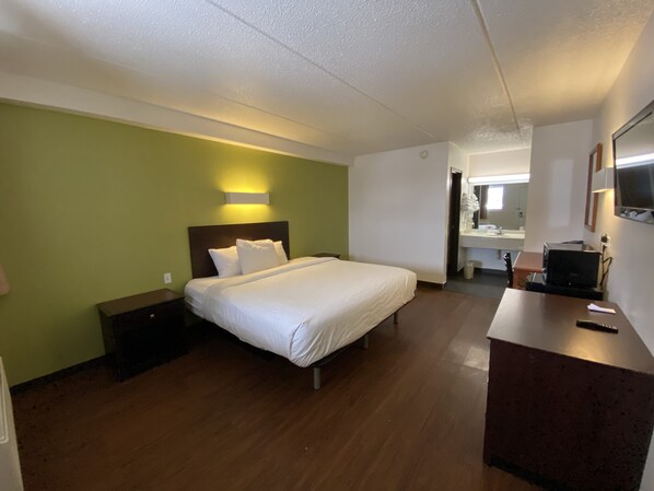 A hotel room with a bed, bedside table, and a desk with a TV.