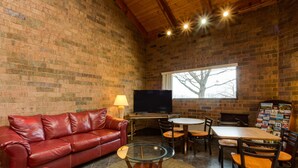 Een gezellige woonkamer met een bakstenen muur, een leren bank, een glazen salontafel, een houten eettafel en stoelen.