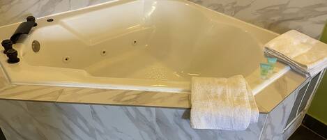 A large, freestanding bathtub with a marble finish, a towel, and a bottle of lotion on the side.