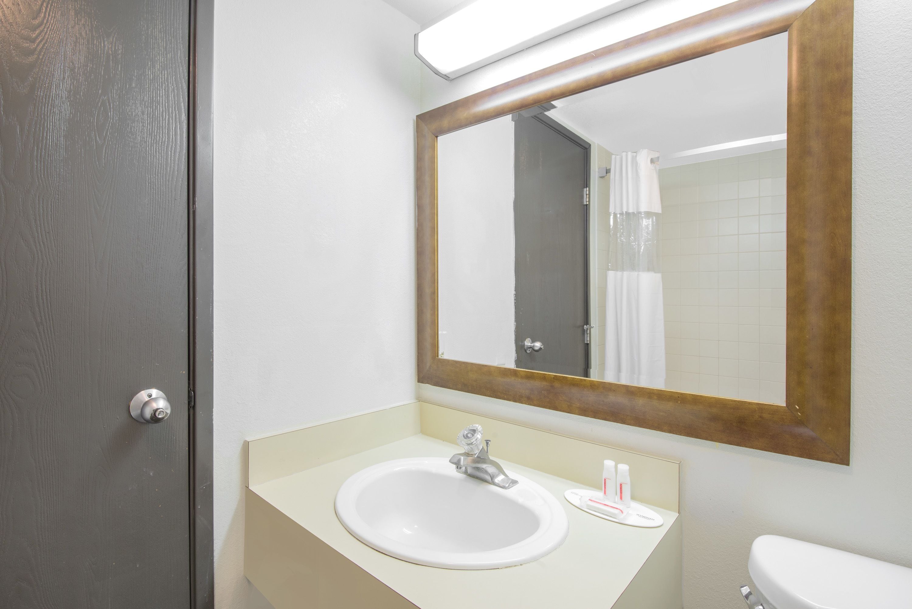 A bathroom with a white sink, a mirror with a wooden frame, a toilet, and a door.