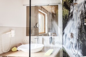 Ein Badezimmer mit einem großen Waschbecken, einem Spiegel, einem Haartrockner und einer Dusche mit einem Wasserfall-Mural.