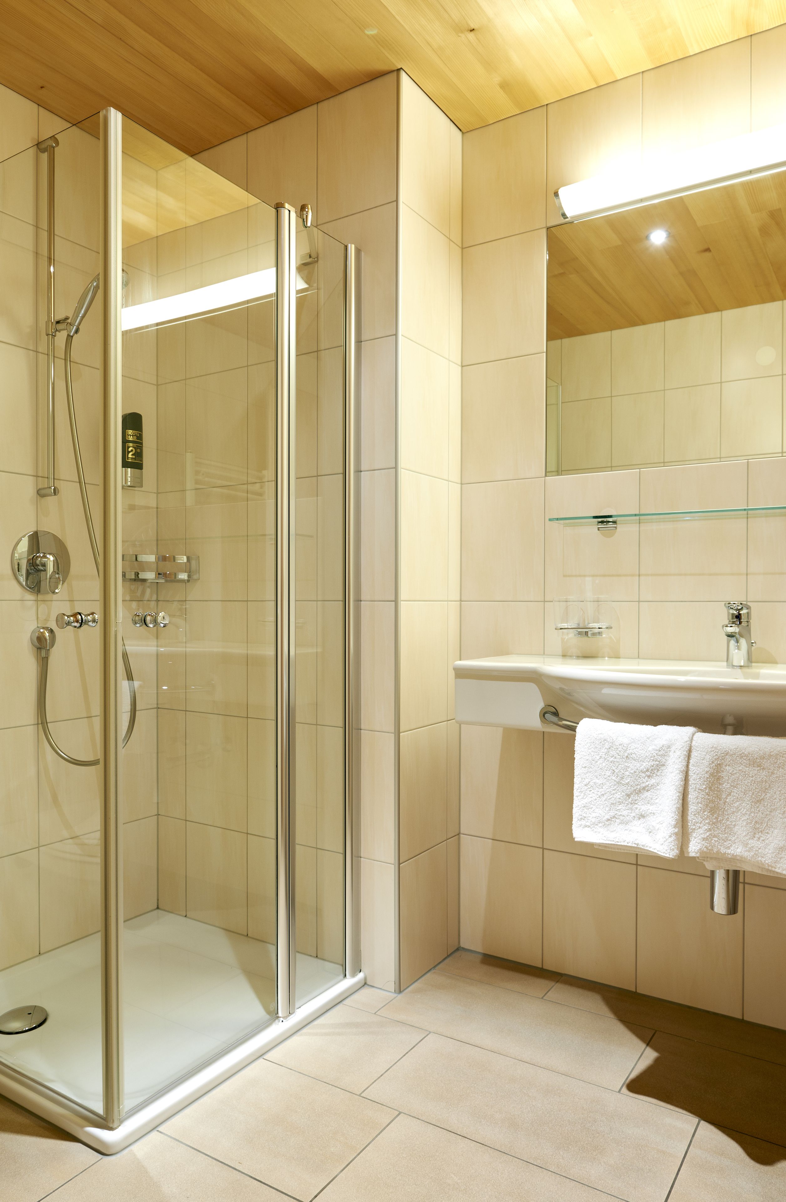 A modern bathroom with a glass-enclosed shower, a sink with a glass shelf, and a mirror above the sink.