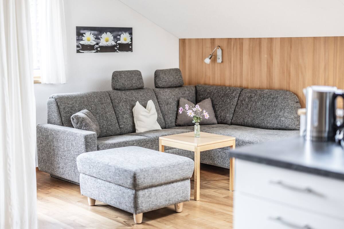 Una sala de estar moderna con un sofá seccional gris, una mesa de centro de madera y un pequeño taburete gris.