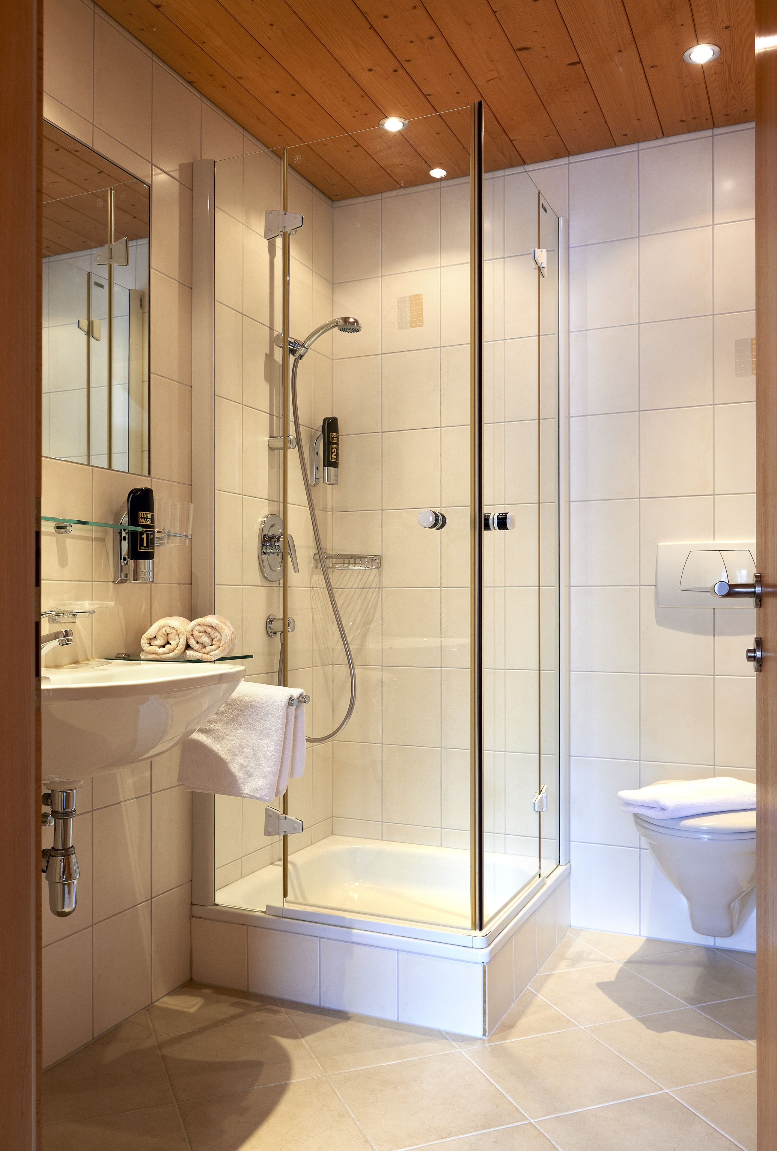 Ein modernes Badezimmer mit einer begehbaren Glasdusche, einer Badewanne, einem Waschbecken mit Glasablage und einer Toilette.