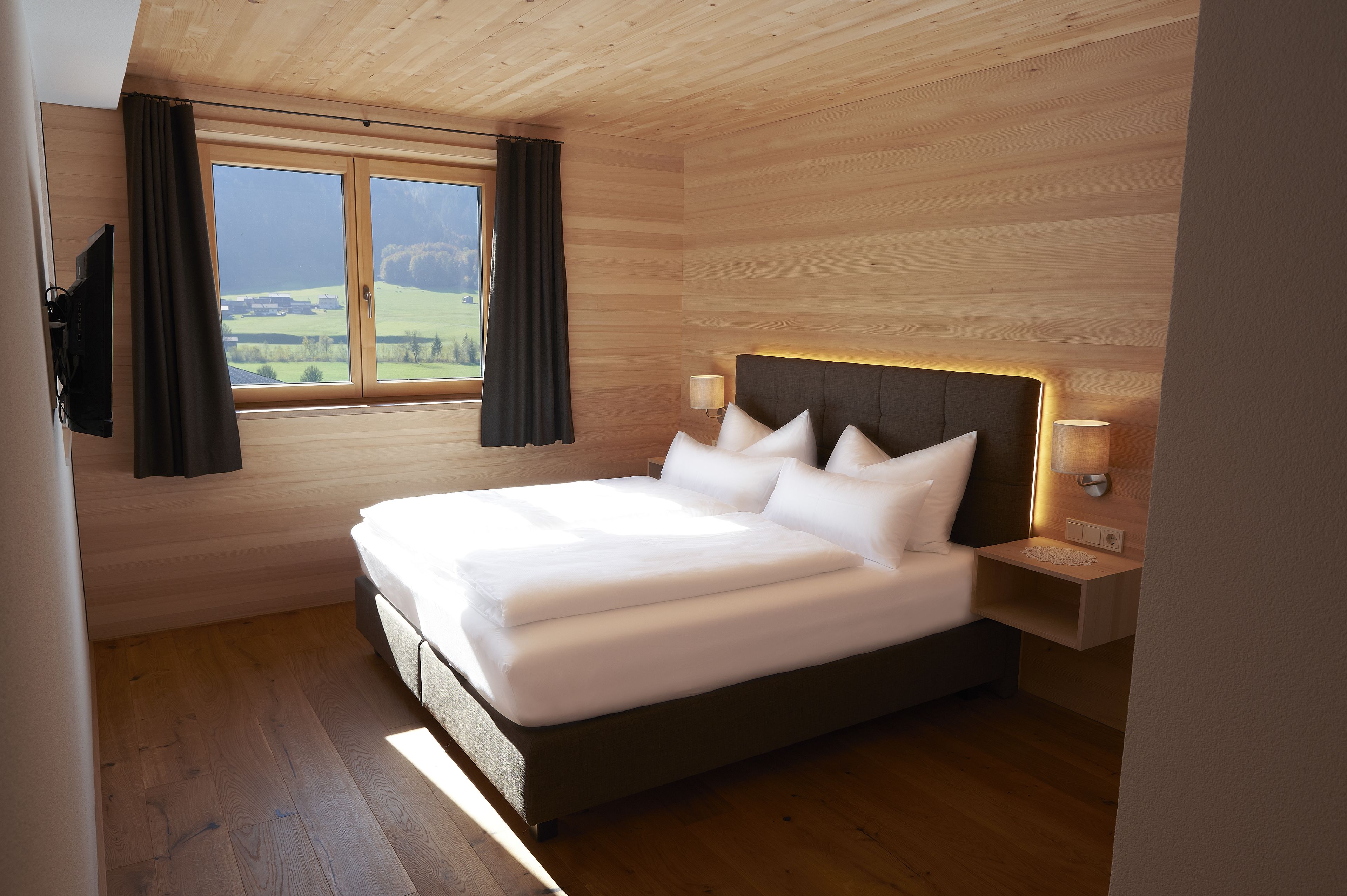 Un dormitorio con una cama grande, paredes de madera, una ventana con cortinas y una mesita de noche con lámpara.