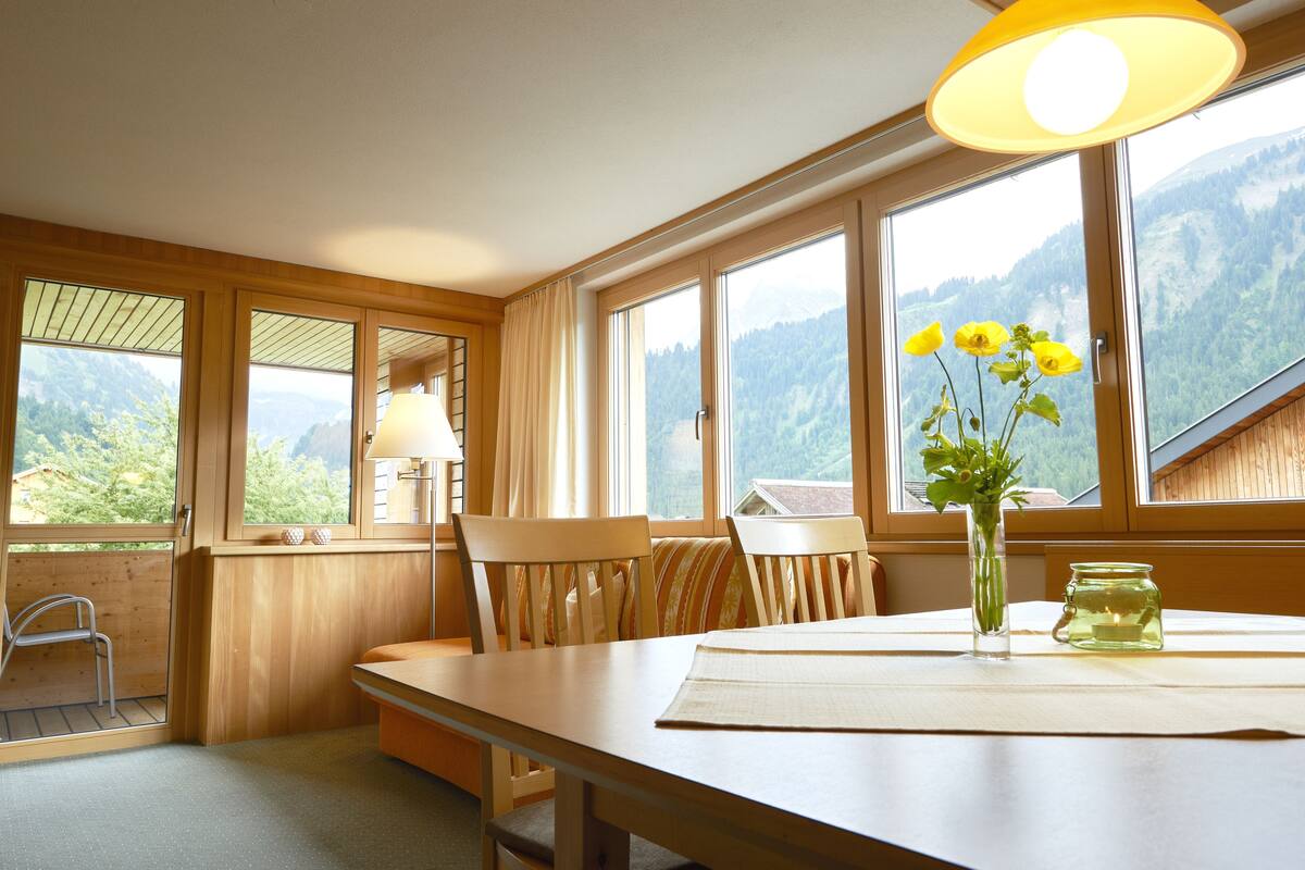 Un interior de madera con una mesa de comedor, sillas, un florero con flores y una vela.