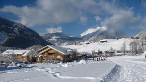 Ein schneebedecktes Bergresort mit Holzhäusern, einer Skipiste und wolkenlosem Himmel.