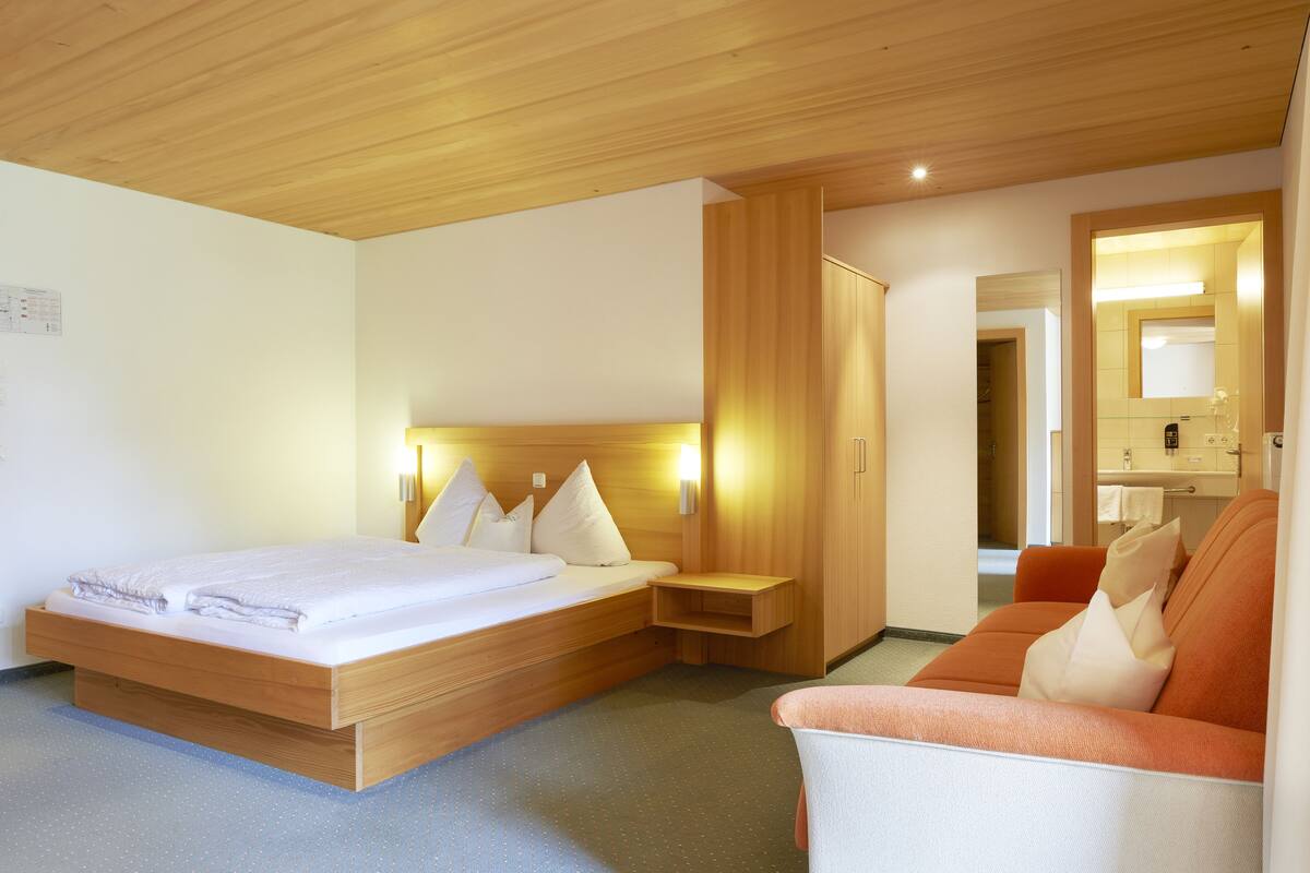 Una habitación de hotel con una cama de madera, un sofá, una mesita de noche y un espejo.