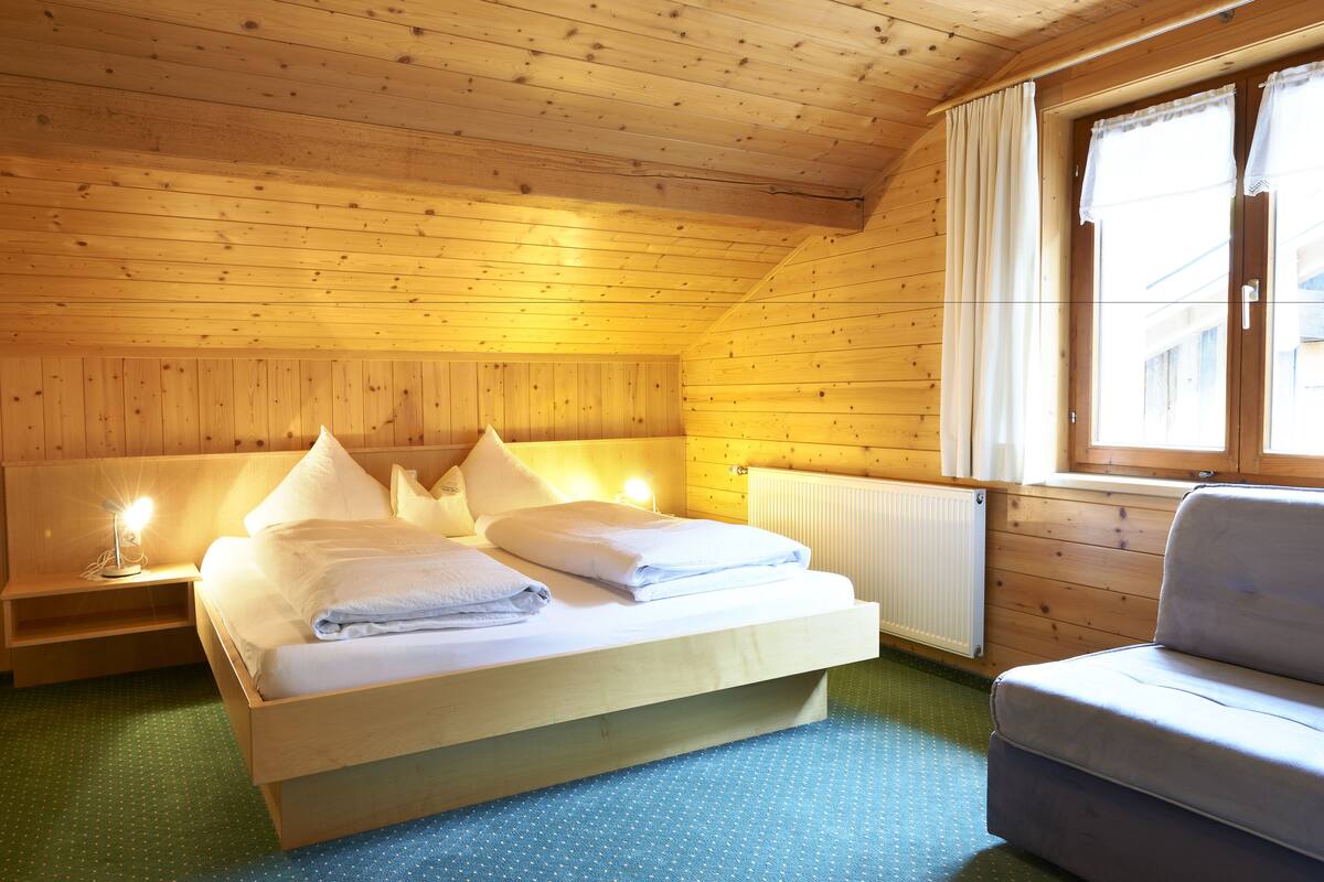 Un dormitorio de cabaña de madera con una cama, lámparas de noche y una ventana.