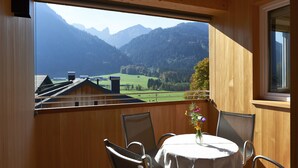 Un balcon en bois, agrémenté d’une table et de chaises, qui offre une vue sur un paysage montagneux sous un ciel dégagé.