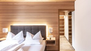 Une chambre d’hôtel moderne avec une tête de lit en bois, un grand lit avec du linge de lit blanc, des tables de chevet avec des lampes et une bibliothèque intégrée.